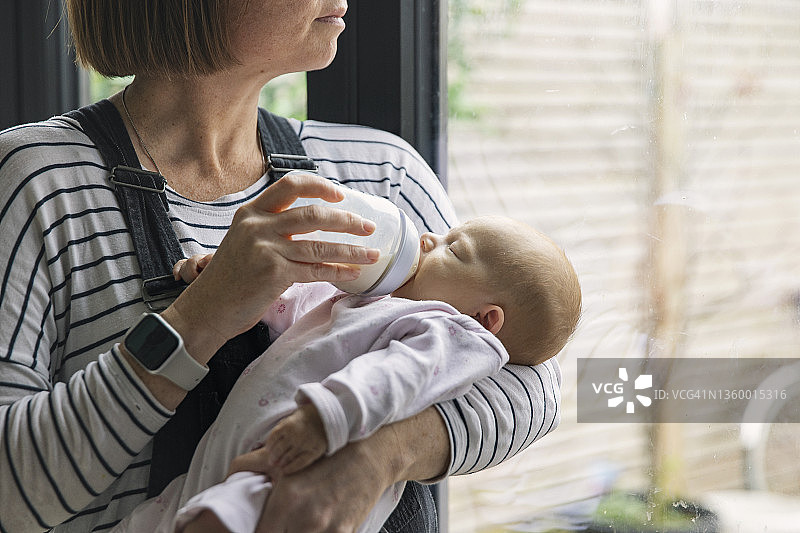中年母亲一边给宝宝喂奶，一边看着窗外图片素材