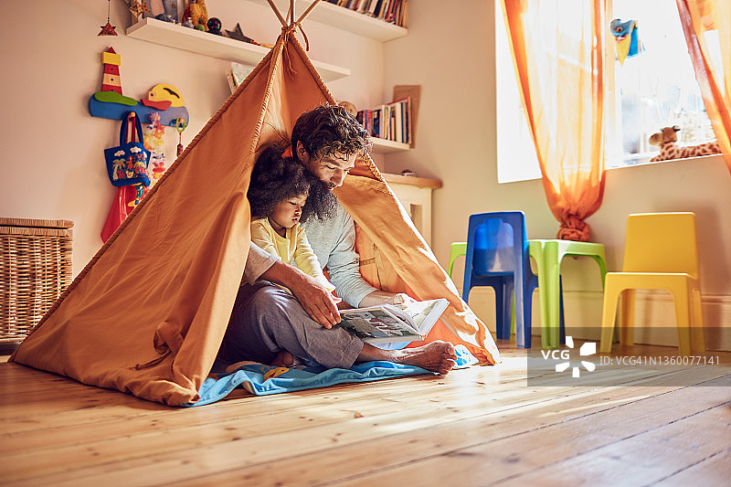 父亲和幼儿女儿在帐篷里读书图片素材