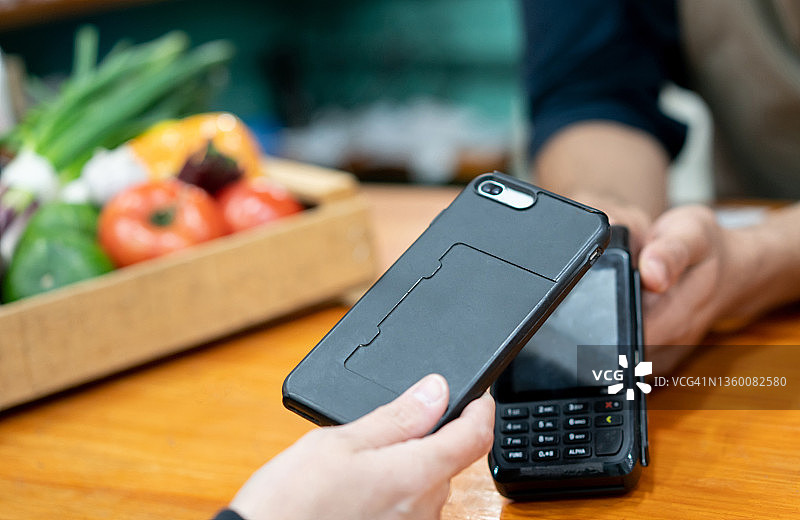 身份不明的顾客用智能手机进行非接触式支付，销售人员拿着信用卡读卡器图片素材