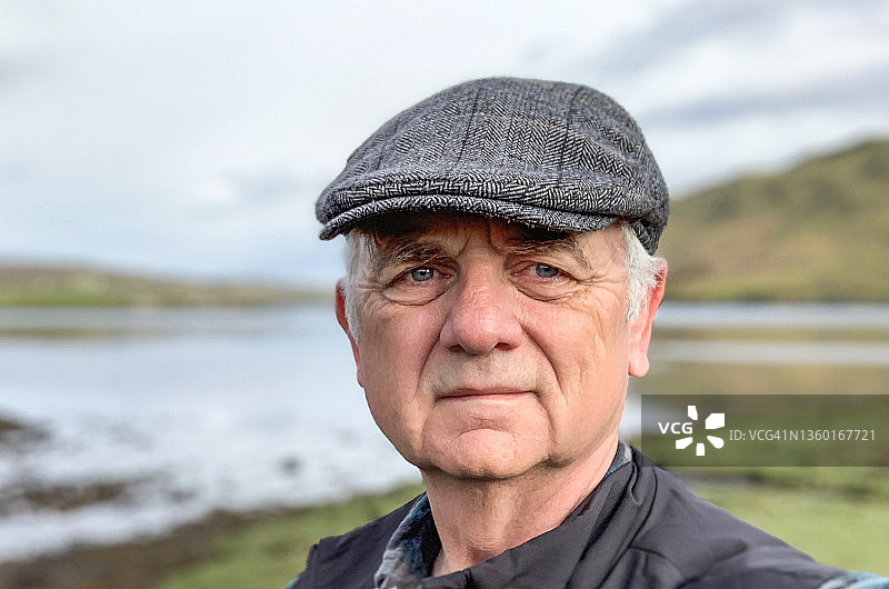 戴着扁帽站在苏格兰斯凯岛乡村景观中的男人肖像图片素材