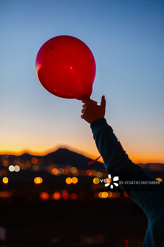 一个人在黄昏时放飞一个红色气球图片素材