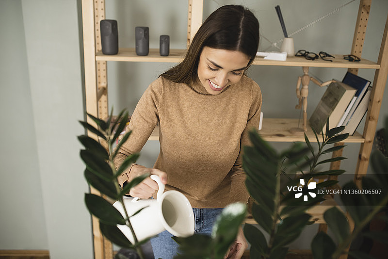 一位面带微笑的女士在客厅里浇花图片素材