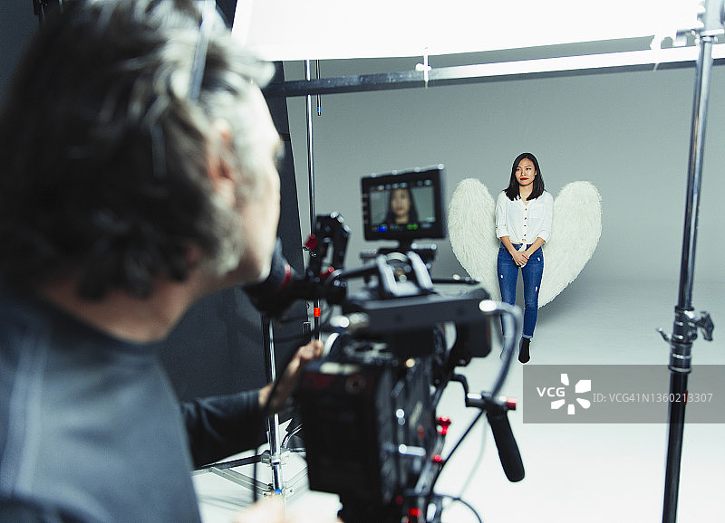 摄影师在相机后拍摄佩戴天使翅膀的年轻女人图片素材