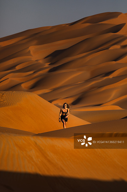 白天，女性走过迪拜的沙漠沙丘，阿拉伯联合酋长国图片素材