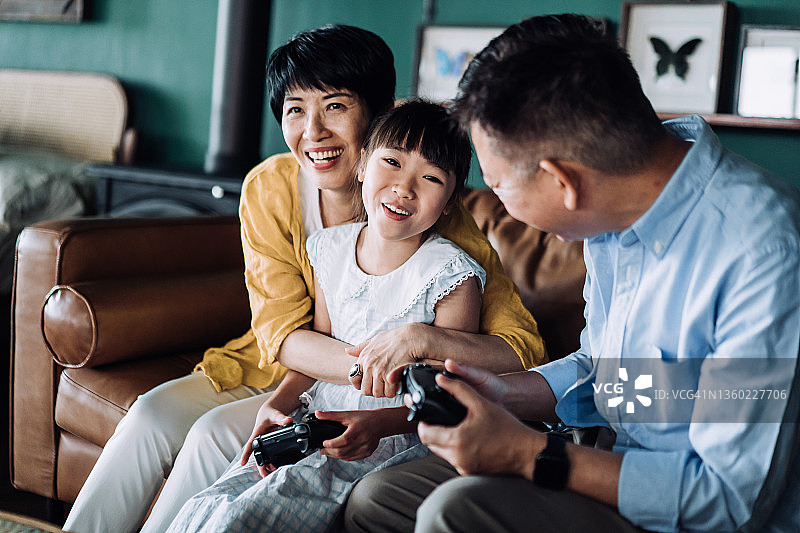 快乐的亚洲祖父母和孙女在家中客厅的沙发上一起玩电子游戏图片素材