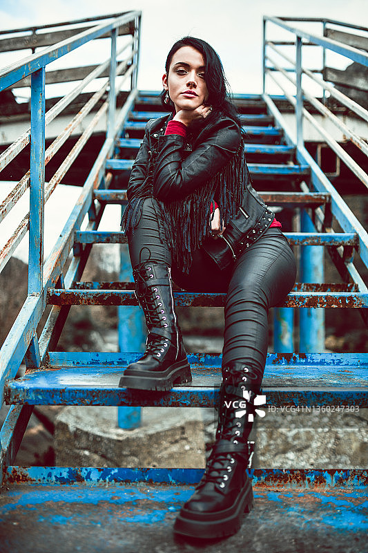 穿着皮衣在生锈的楼梯上休息的美丽哥特风女人图片素材
