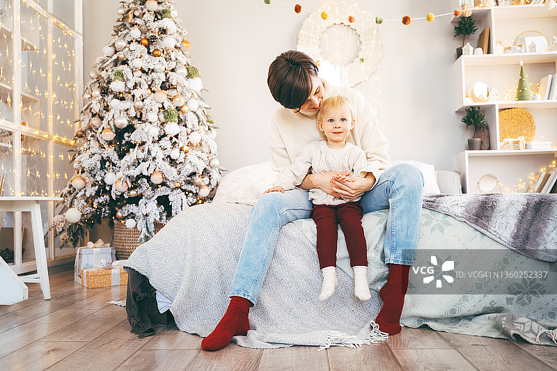 圣诞装饰房间里，坐在妈妈腿上的小宝宝看着镜头图片素材