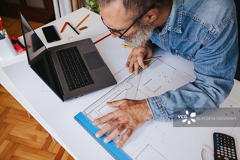 在中年男人在家庭办公室工作，有建筑图纸图片素材