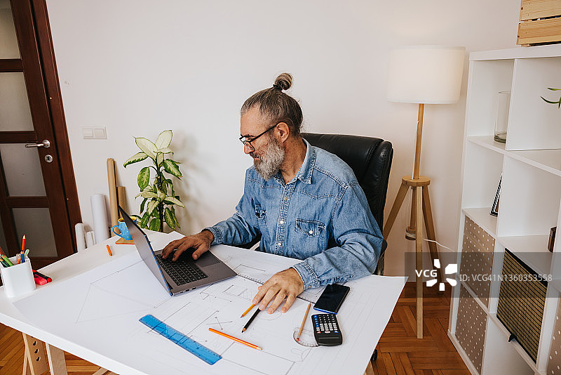 年长的男建筑师在家用蓝图和笔记本电脑工作图片素材