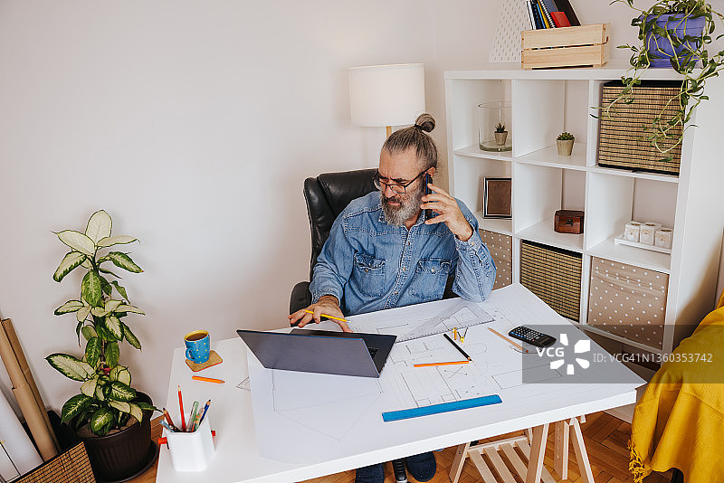 在家办公时使用手机的成熟男工程师图片素材