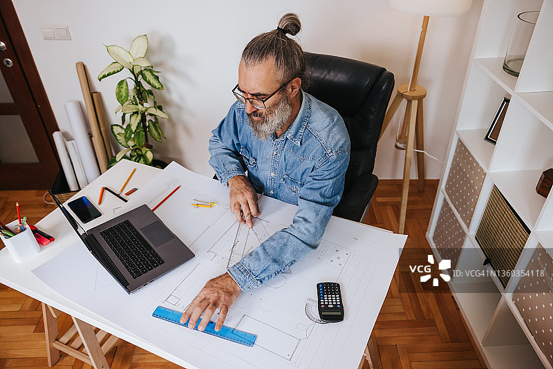 年长的建筑师在家中办公室绘制蓝图图片素材