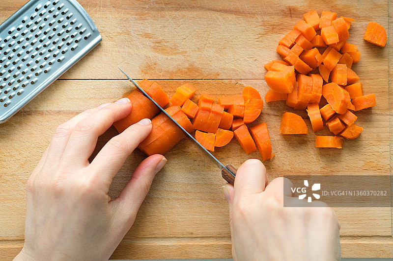 女人将煮熟的胡萝卜切成丁，准备蔬菜沙拉，案板上的菜刀，附近有其他食材，素食主义概念图片素材