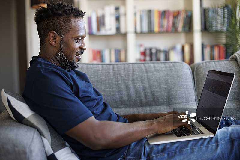 坐在沙发上使用笔记本电脑的放松微笑的男人图片素材
