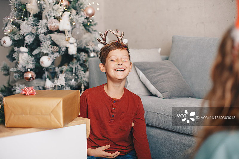 微笑的男孩坐在客厅的地板上，玩耍并和他的妹妹说话，圣诞节图片素材