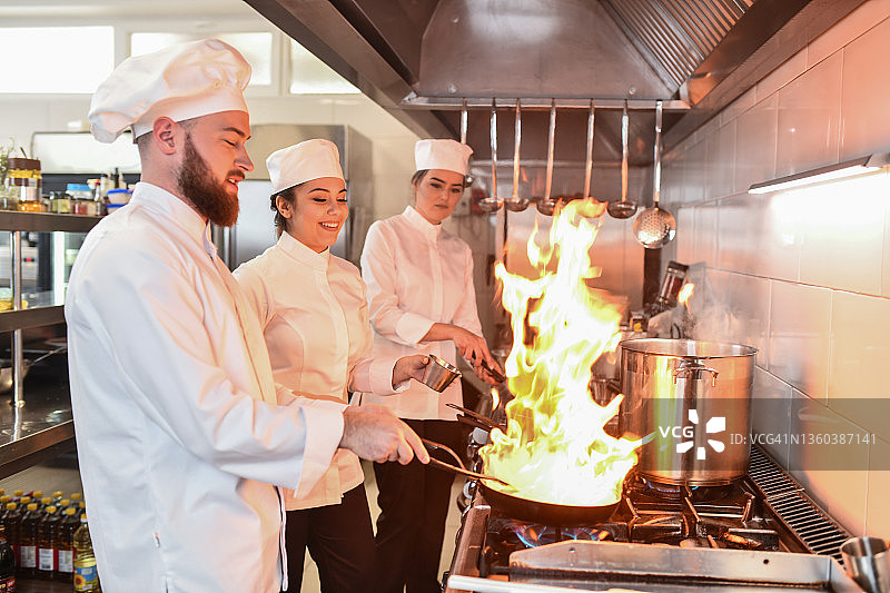 男厨师为女厨师展示煎锅中的火焰图片素材