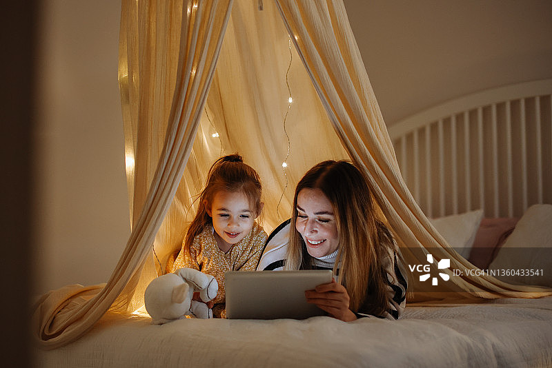 母女在床上帐篷里一起看平板电脑图片素材