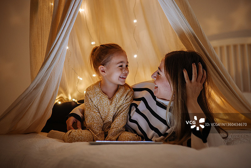 母女在床上帐篷里一起看平板电脑图片素材