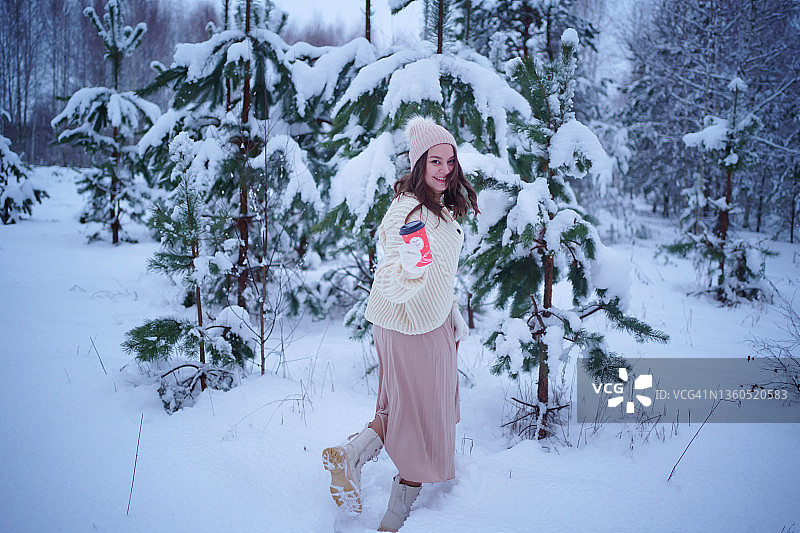 圣诞节：手捧咖啡走在冬季森林中的女孩图片素材