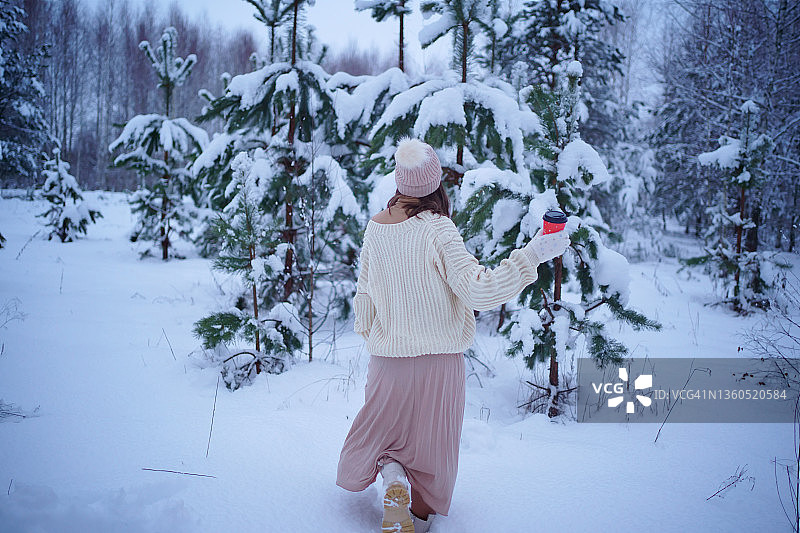 圣诞节：手捧咖啡走在冬季森林中的女孩图片素材