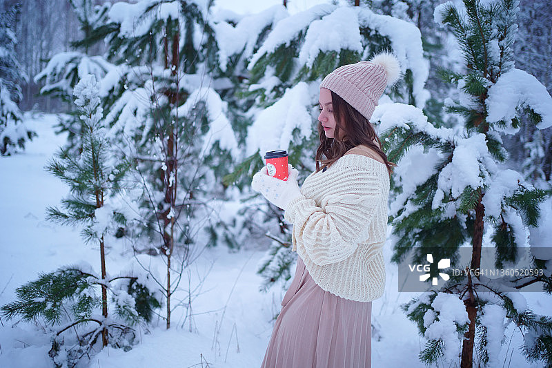 圣诞节：手捧咖啡走在冬季森林中的女孩图片素材