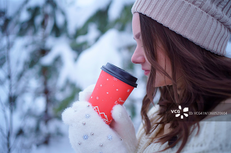 戴帽子的女孩拿着红色咖啡杯，圣诞雪景森林图片素材