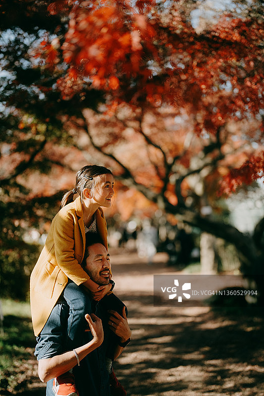 父亲肩扛女儿，背景是红色枫叶图片素材