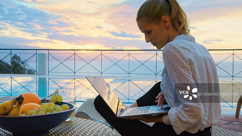 在露台上使用笔记本电脑欣赏海景的女人图片素材