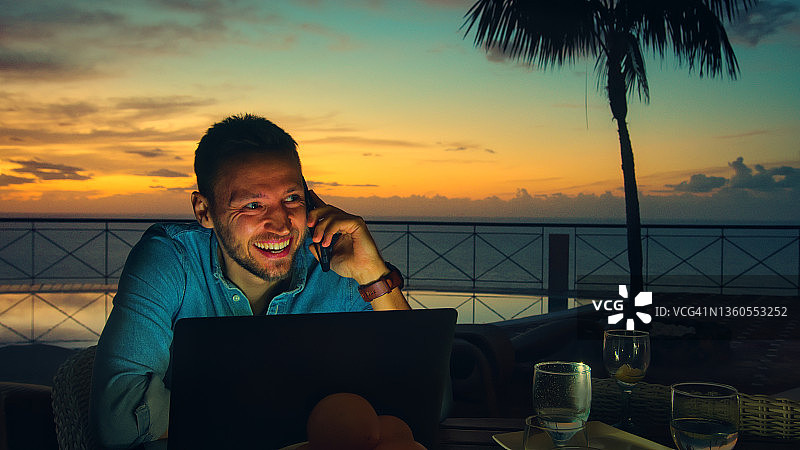 男人在露台上工作，在壮丽的海上日落时进行视频通话图片素材