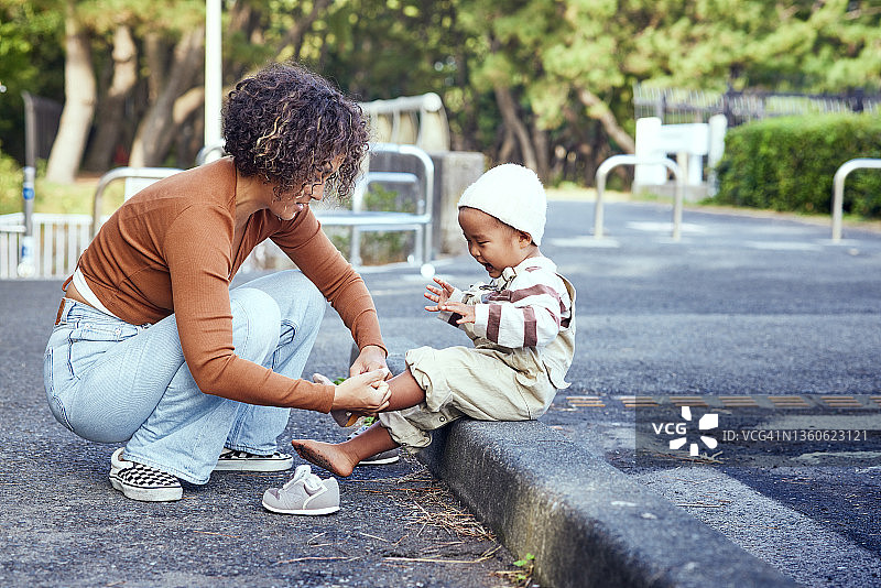 母亲坐在路边帮助年幼的儿子穿鞋图片素材
