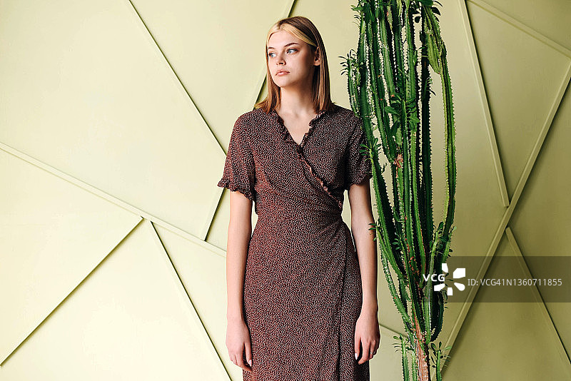 浅色背景下，女孩站在一个大仙人掌旁。图片素材