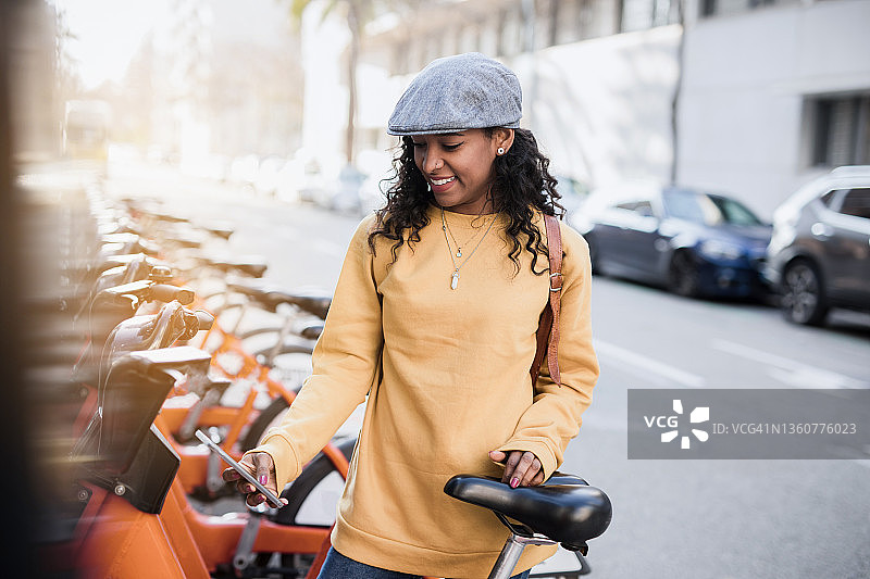一位年轻的黑人妇女正在使用智能手机扫描城市里共享单车的二维码图片素材