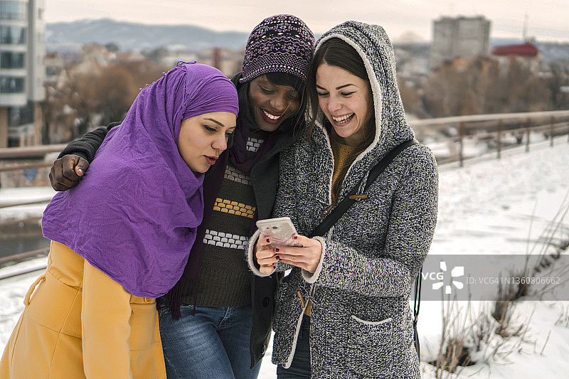 冬天在户外看手机的多民族女性朋友群体图片素材
