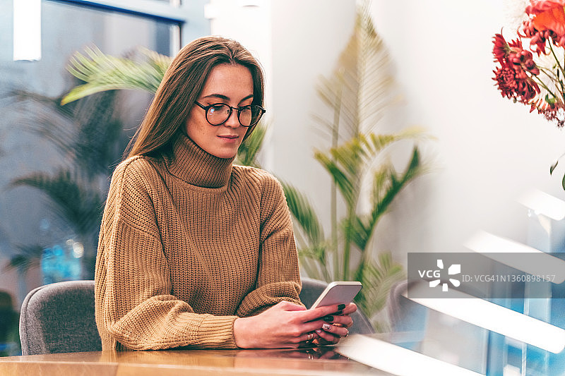 戴着时尚眼镜的年轻女商人正在用手机发短信图片素材