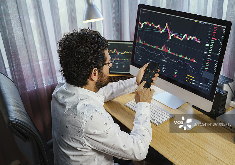 商人在家分析电脑和笔记本电脑屏幕上的加密货币市场图表。比特币/加密货币概念图片素材
