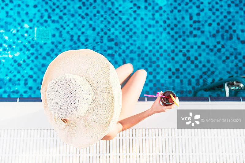戴帽美女在泳池边喝鸡尾酒图片素材