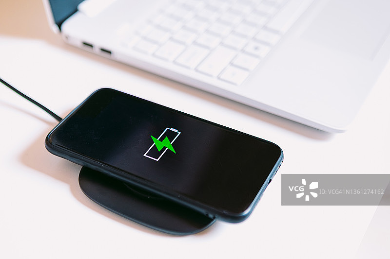 黑色手机在充电座上充电，旁边是笔记本电脑图片素材