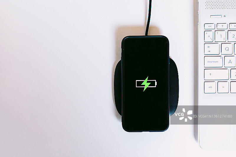 黑色手机在充电座上充电，旁边是笔记本电脑图片素材