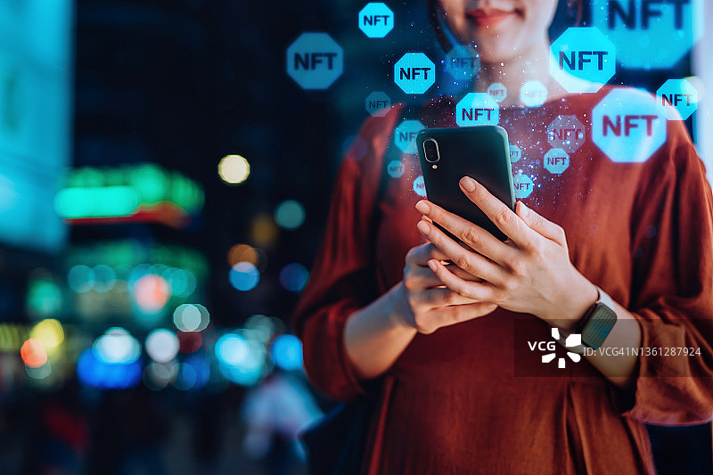 年轻亚洲女性在市中心街道夜晚使用智能手机，研究区块链技术，投资或交易加密货币、数字资产、艺术作品和数字账本的近景图片素材