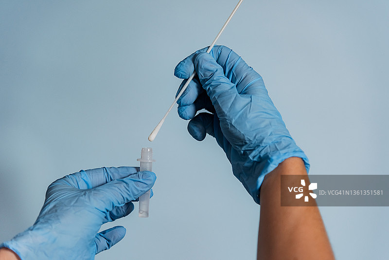 戴着蓝色外科手套的医护人员将棉签插入提取管中图片素材