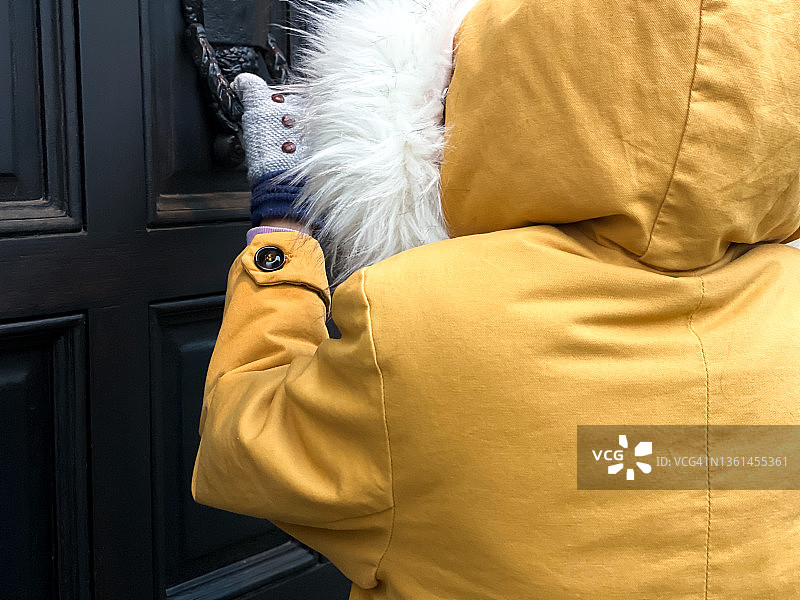 身穿明黄色冬装的年轻女子敲击住宅前门图片素材