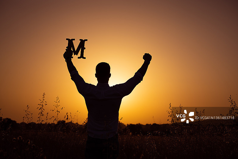 举起手臂，手中拿着字母M的男人轮廓的背影图片素材