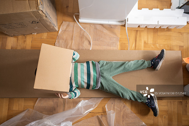男孩躺在新房的地板上，面前拿着纸板图片素材