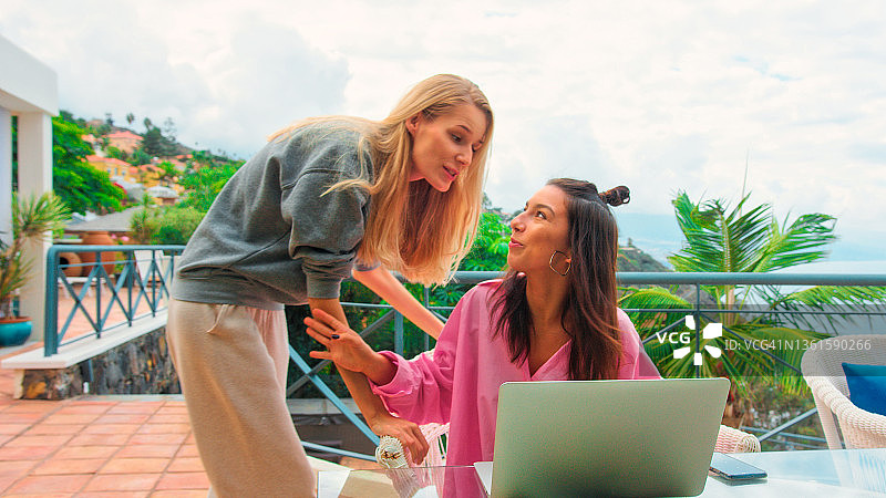 在热带气候的露台上使用笔记本电脑工作的女人，因同事打断重要的商务电话图片素材