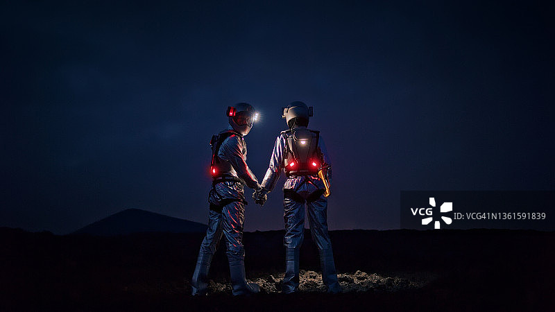 与众不同的自拍：身穿未来主义发光宇航服的宇航员手牵手拍照图片素材