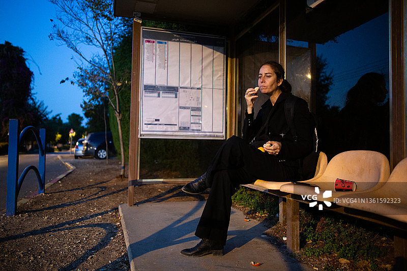 女人在巴士站等候时吃东西图片素材