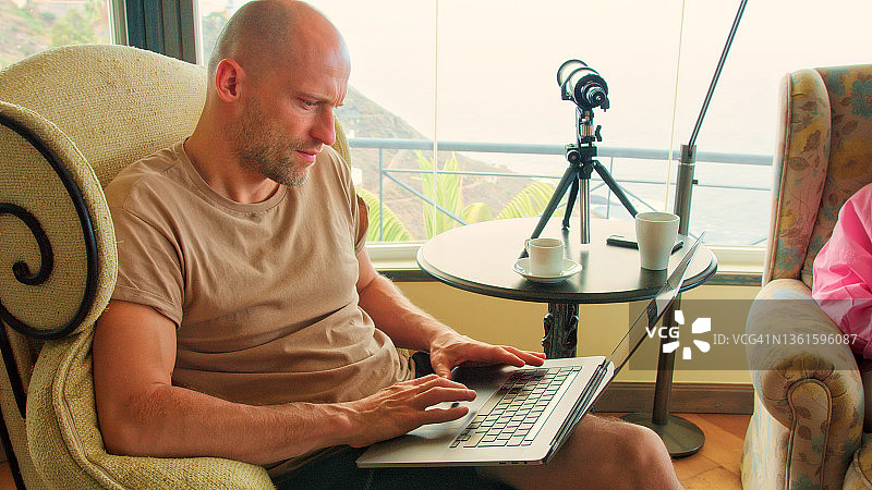 同事们坐在全景窗边，使用笔记本电脑喝咖啡，欣赏壮丽的海景，在工作期间聊天欢笑图片素材