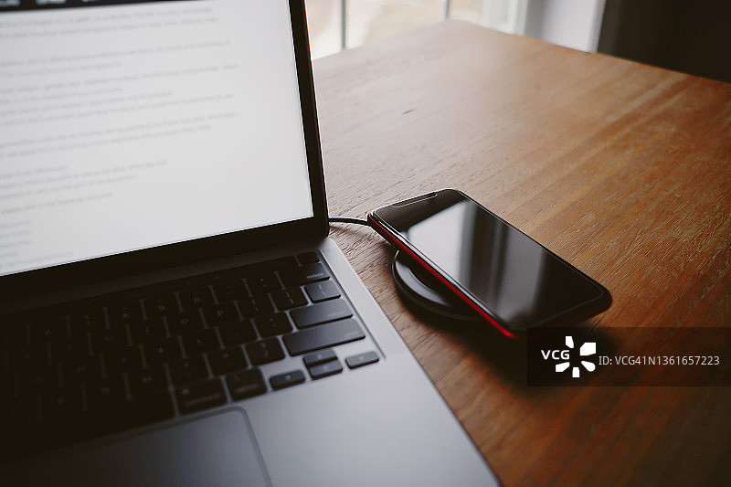 办公桌上的笔记本电脑和无线充电智能手机图片素材