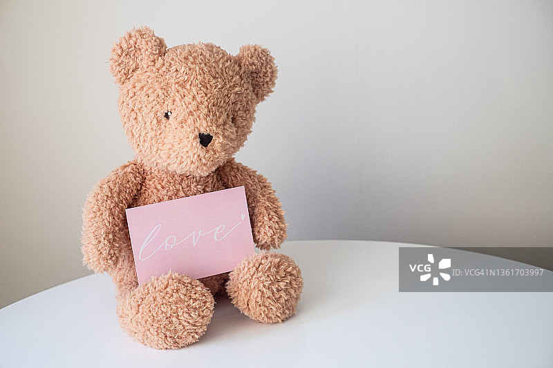 可爱的泰迪熊拿着爱心明信片，选择性聚焦。情人节贺卡图片素材