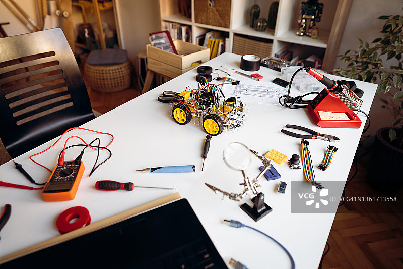 堆满电子设备的杂乱桌面，机器人工程师正在制造机器人汽车图片素材