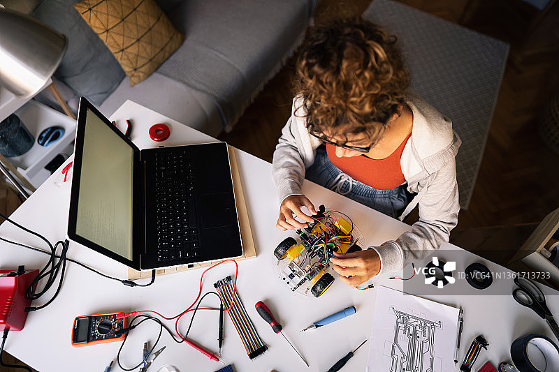 女性理工科学生在创意工作室里调试带传感器的自动驾驶机器人汽车图片素材